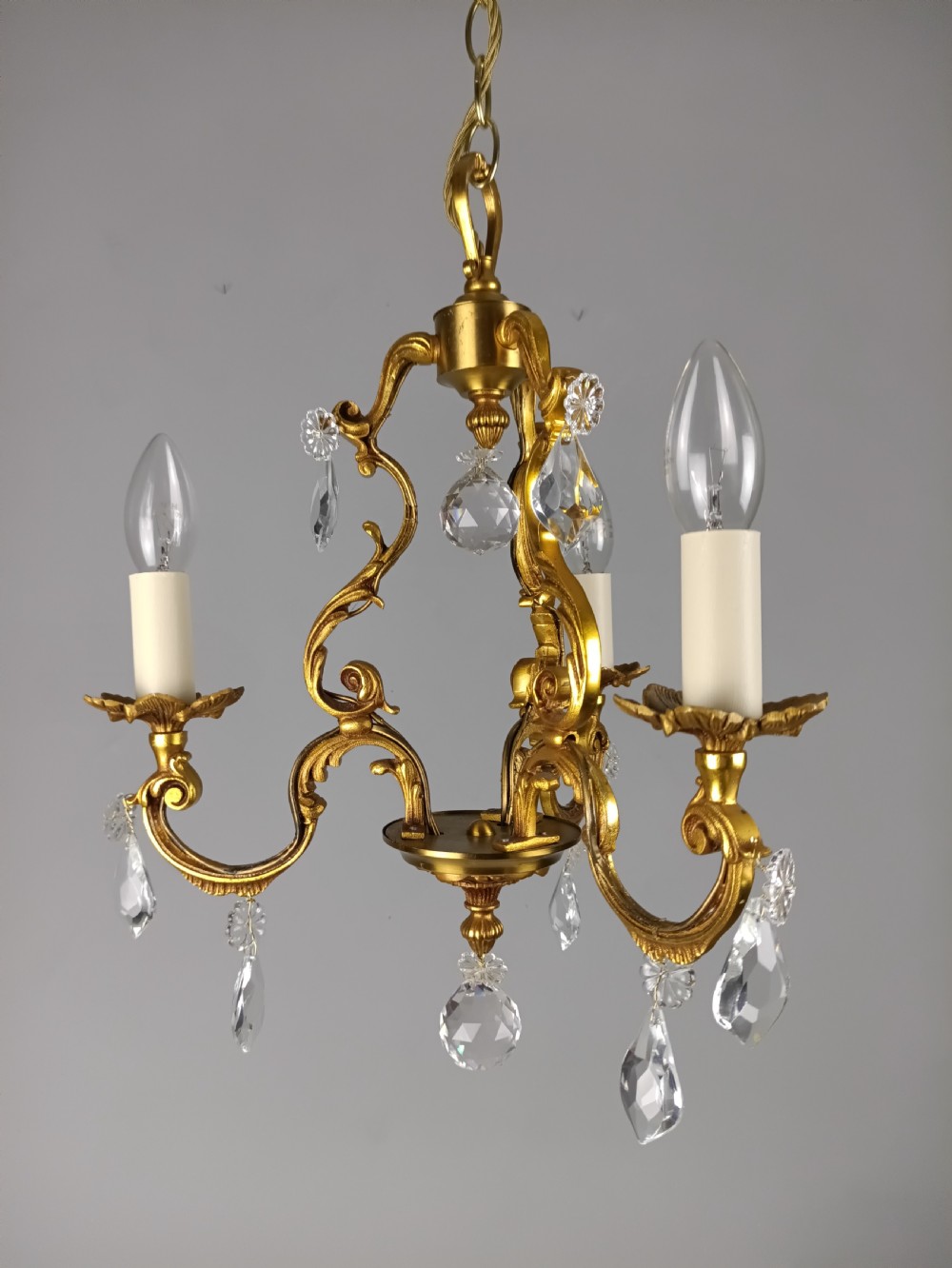 A three-arm French gilt brass chandelier decorated with scrolling foliate branches, candle sleeves, and faceted crystal glass drops. View XIV