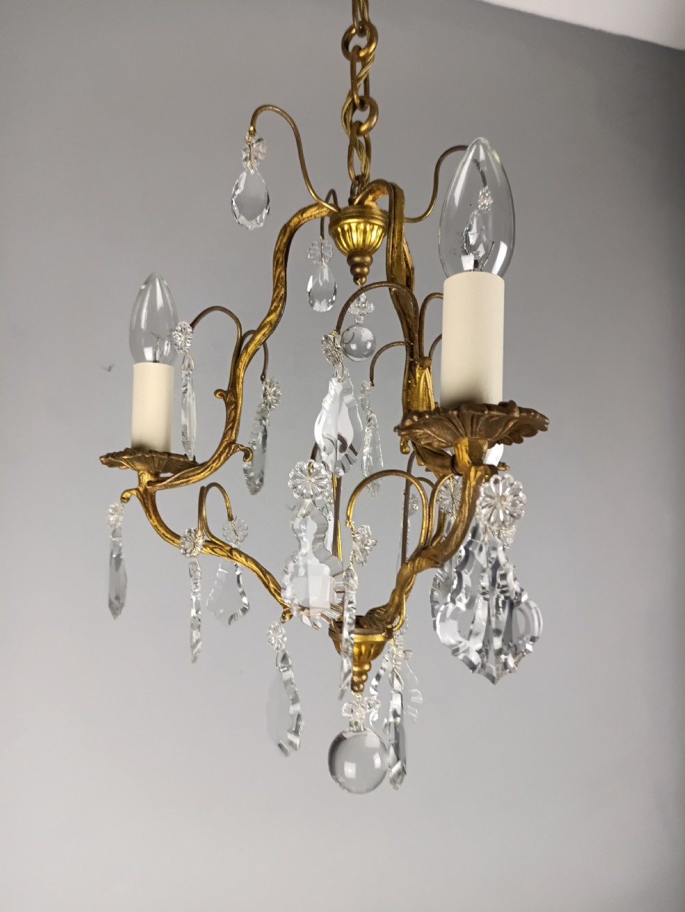 An antique French gilt brass three-light chandelier featuring curved scrolling arms, cream candle-style sleeves, and faceted crystal drops. View II