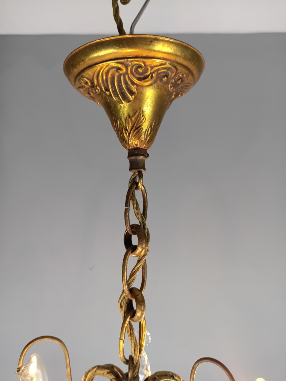 An antique French gilt brass three-light chandelier featuring curved scrolling arms, cream candle-style sleeves, and faceted crystal drops. View V