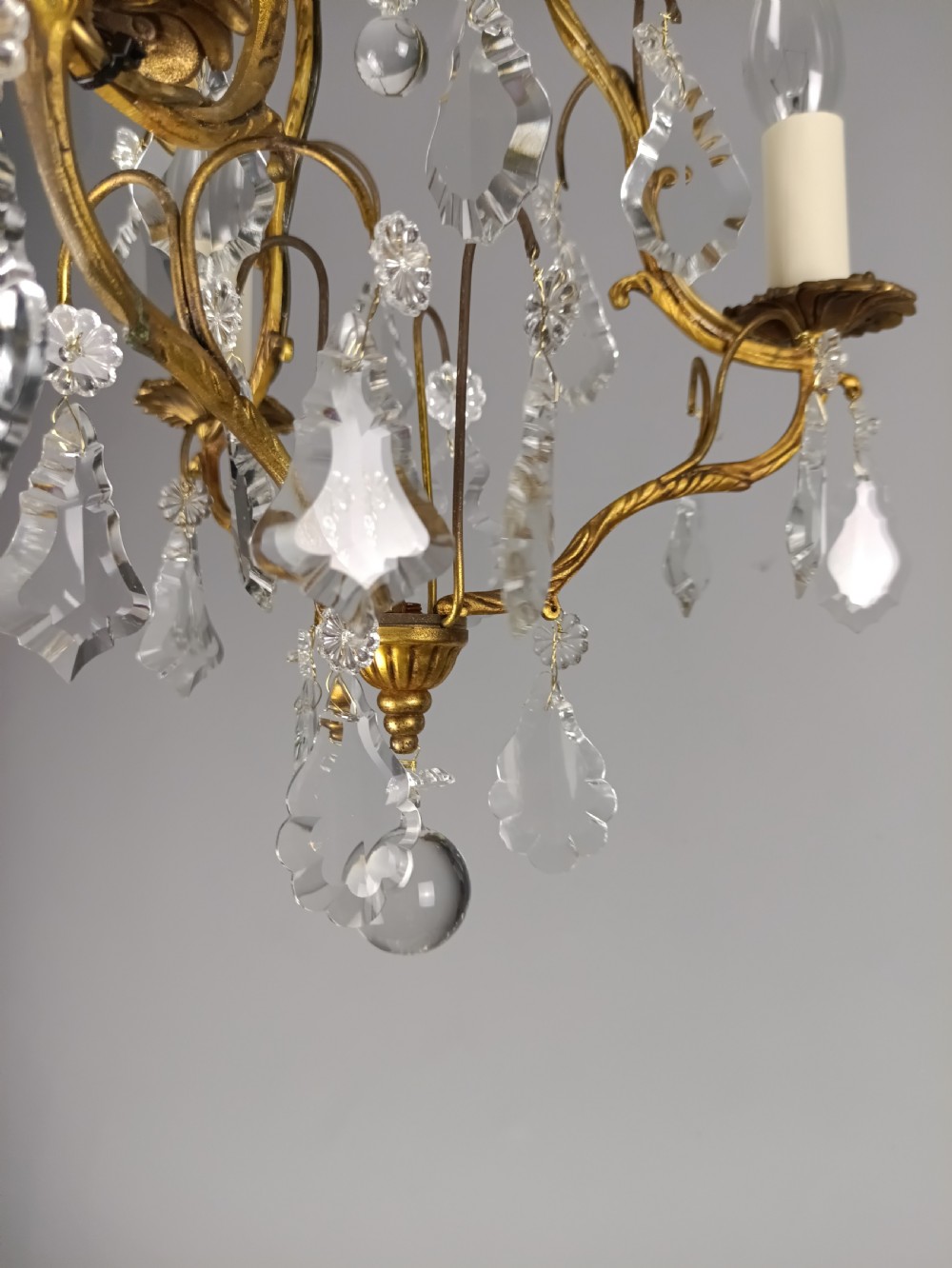 An antique French gilt brass three-light chandelier featuring curved scrolling arms, cream candle-style sleeves, and faceted crystal drops. View IX