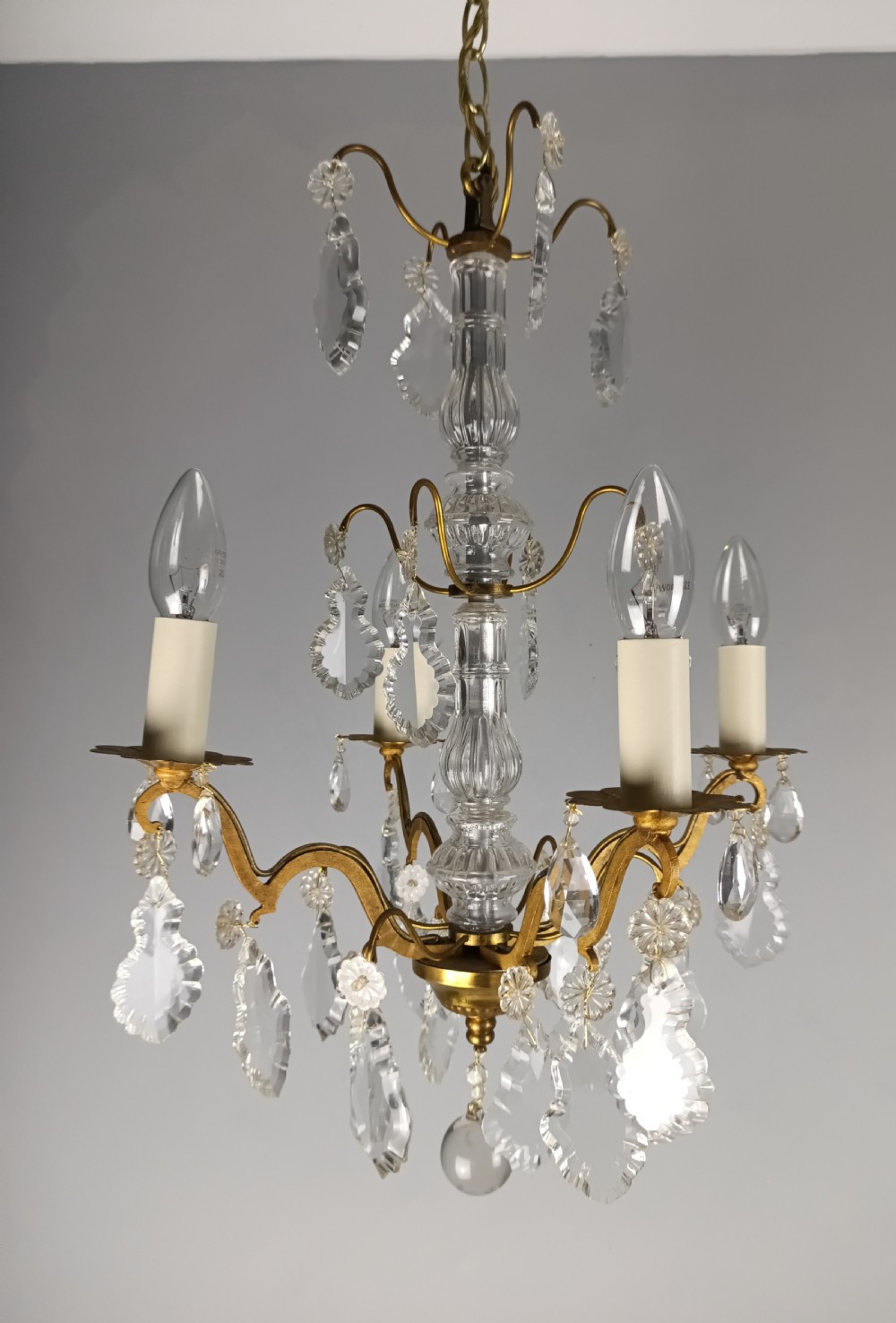 A four-light French gilded brass chandelier featuring a central glass column and hanging cut crystal drops.