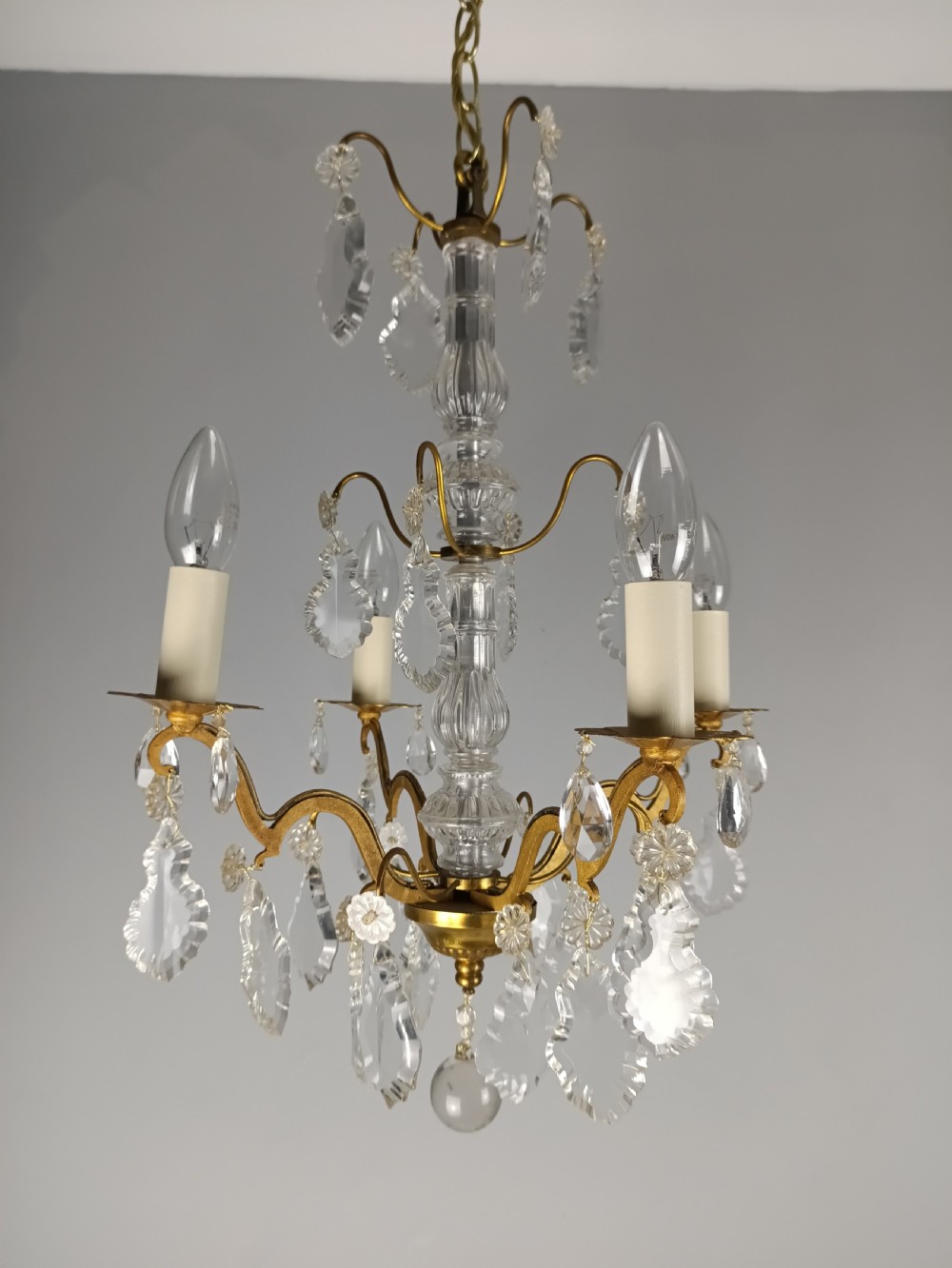 A four-light French gilded brass chandelier featuring a central glass column and hanging cut crystal drops. View V