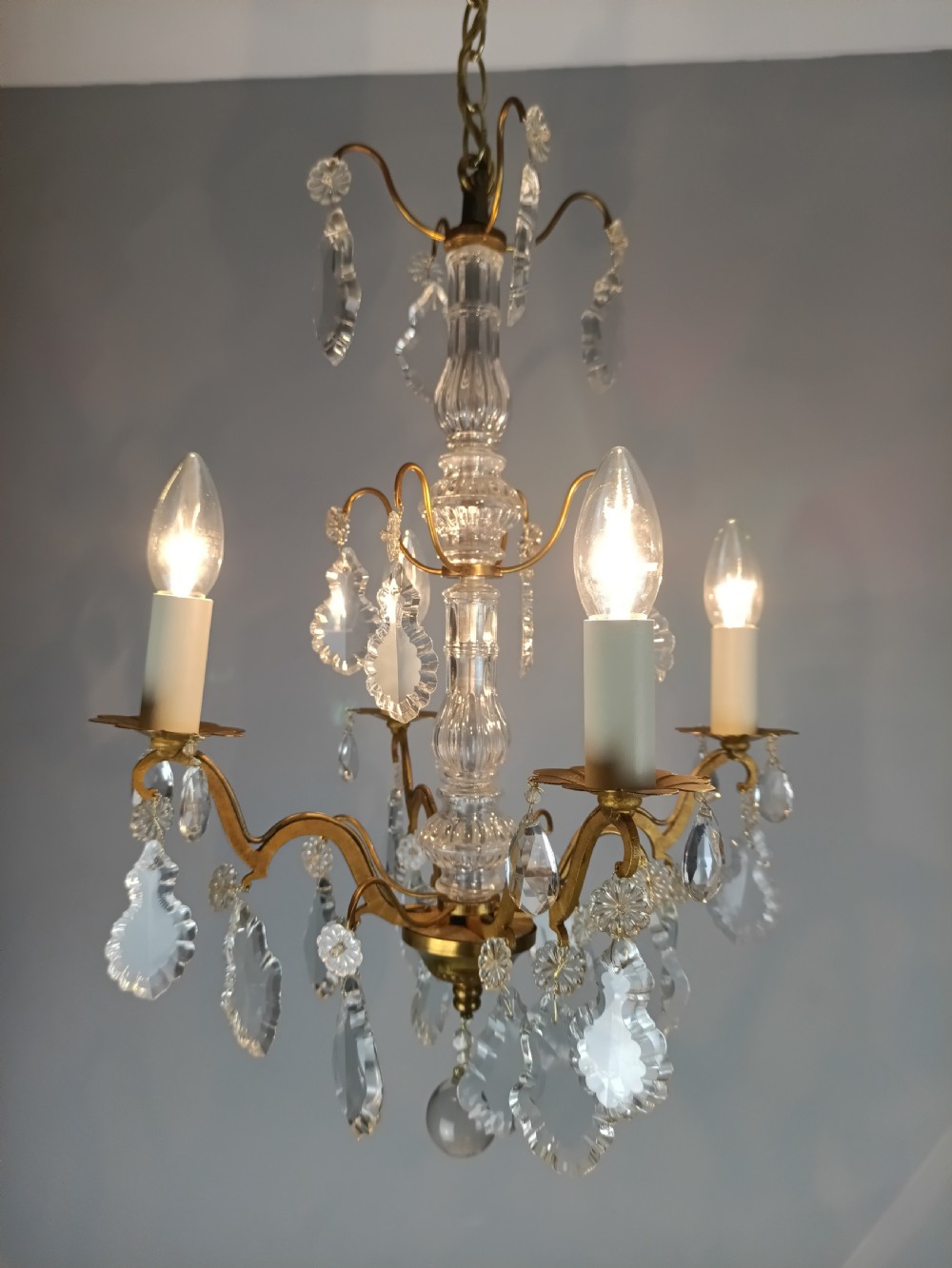 A four-light French gilded brass chandelier featuring a central glass column and hanging cut crystal drops. View VI
