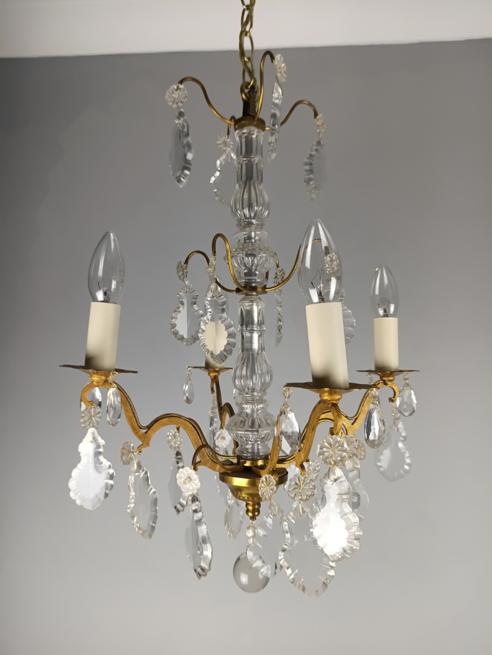 A four-light French gilded brass chandelier featuring a central glass column and hanging cut crystal drops. View VIII