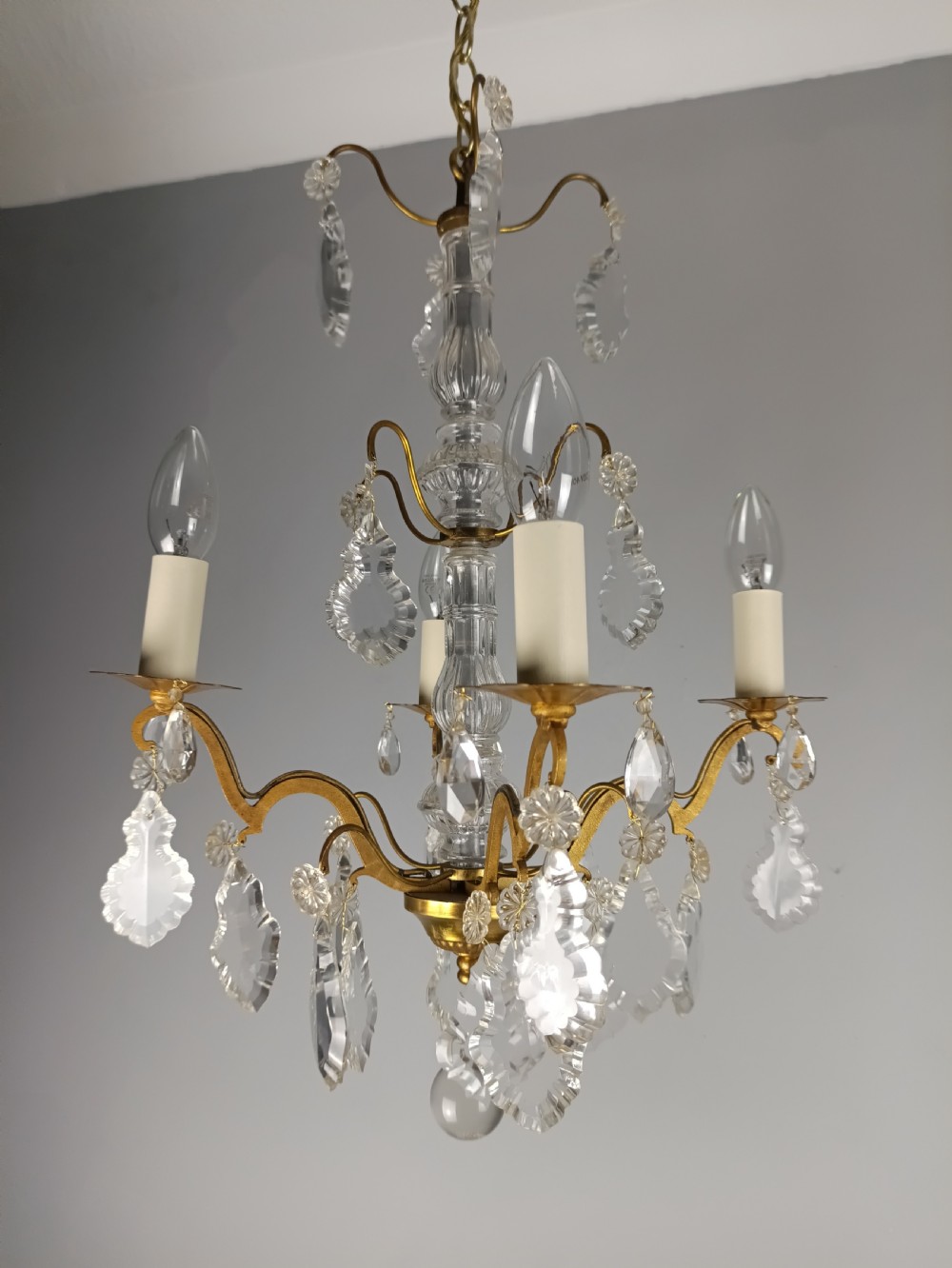 A four-light French gilded brass chandelier featuring a central glass column and hanging cut crystal drops. View IX