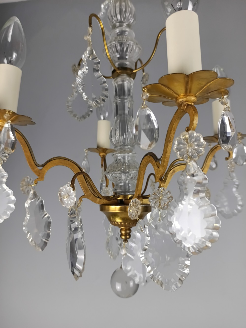 A four-light French gilded brass chandelier featuring a central glass column and hanging cut crystal drops. View X