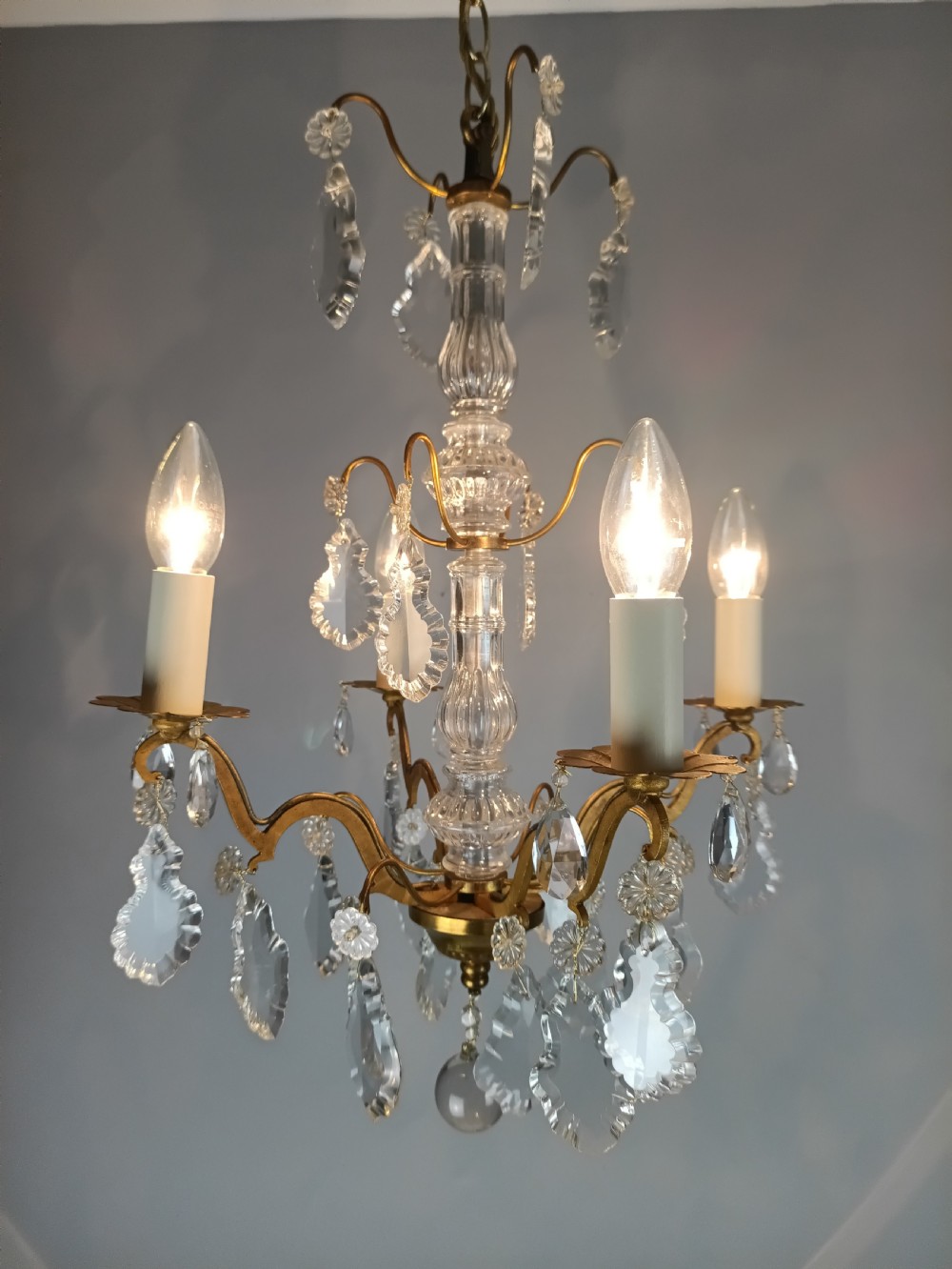 A four-light French gilded brass chandelier featuring a central glass column and hanging cut crystal drops. View XI