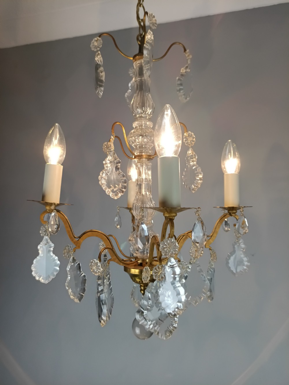 A four-light French gilded brass chandelier featuring a central glass column and hanging cut crystal drops. View XII