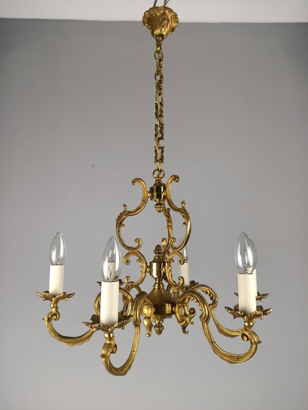 A six-arm French gilt brass chandelier featuring ornate acanthus scrollwork and white candle-style light sockets. View II
