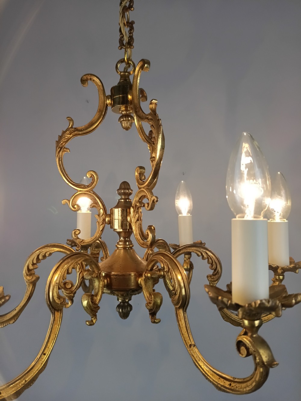 A six-arm French gilt brass chandelier featuring ornate acanthus scrollwork and white candle-style light sockets. View III