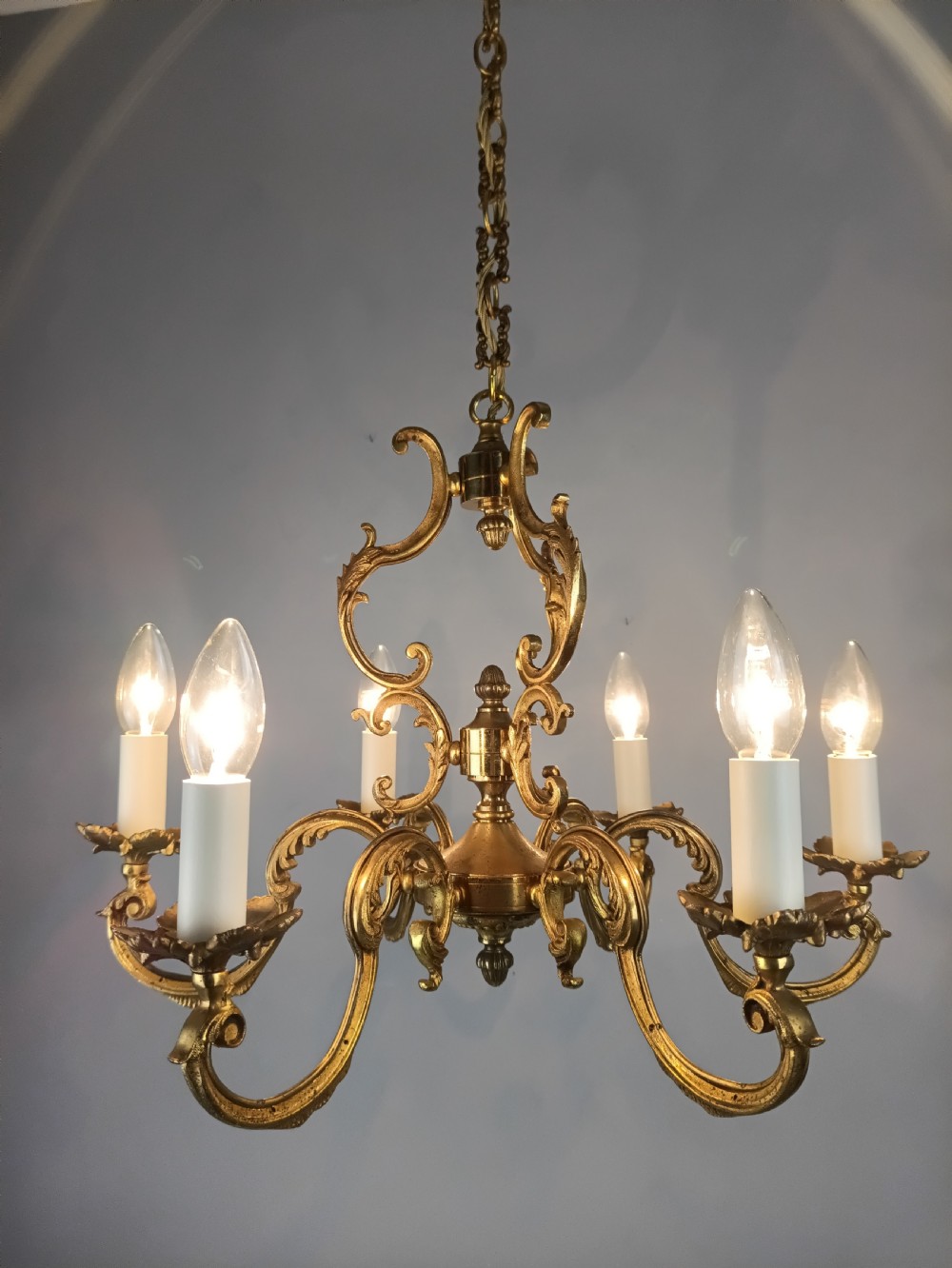 A six-arm French gilt brass chandelier featuring ornate acanthus scrollwork and white candle-style light sockets. View IV