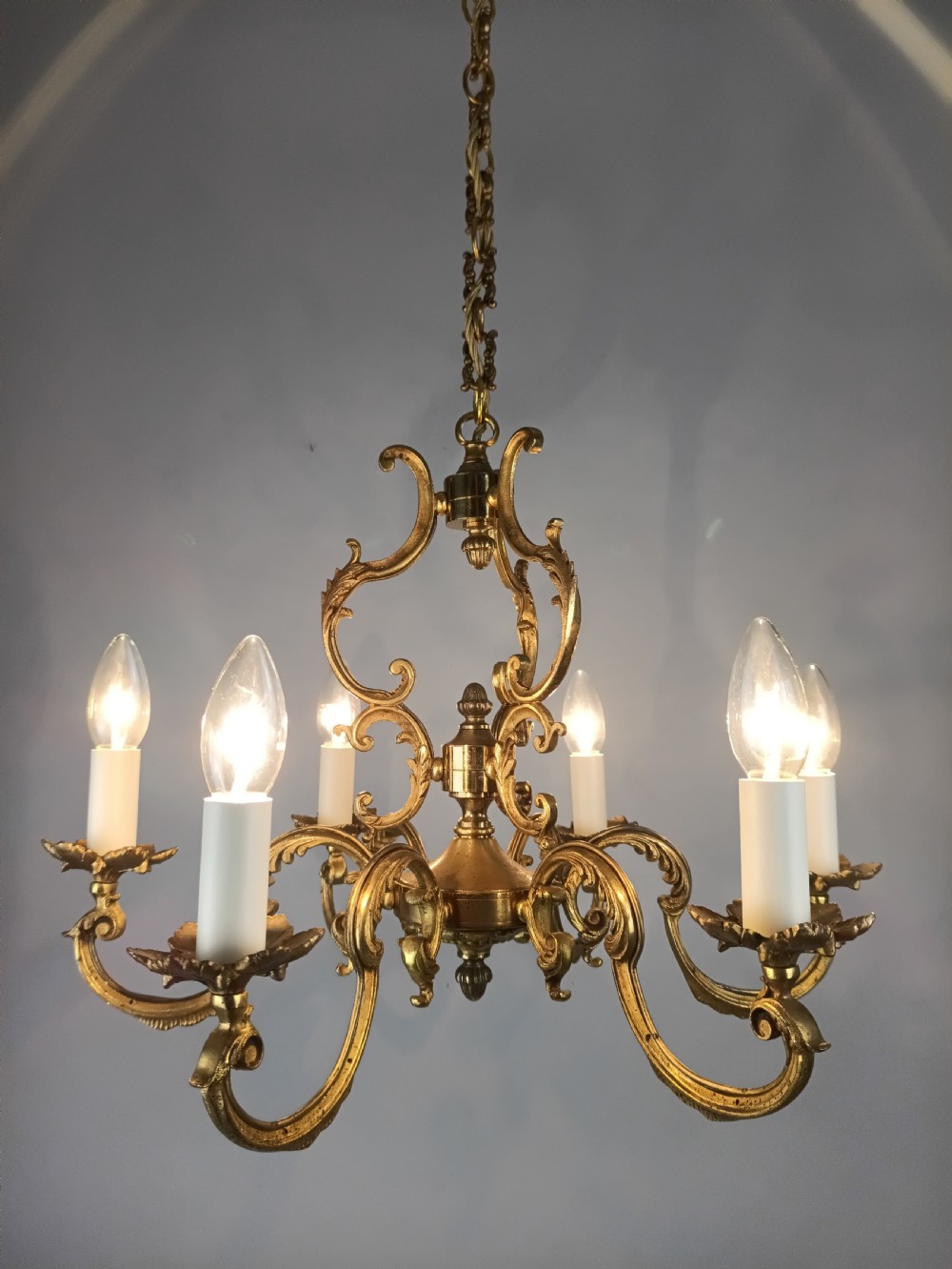 A six-arm French gilt brass chandelier featuring ornate acanthus scrollwork and white candle-style light sockets. View V