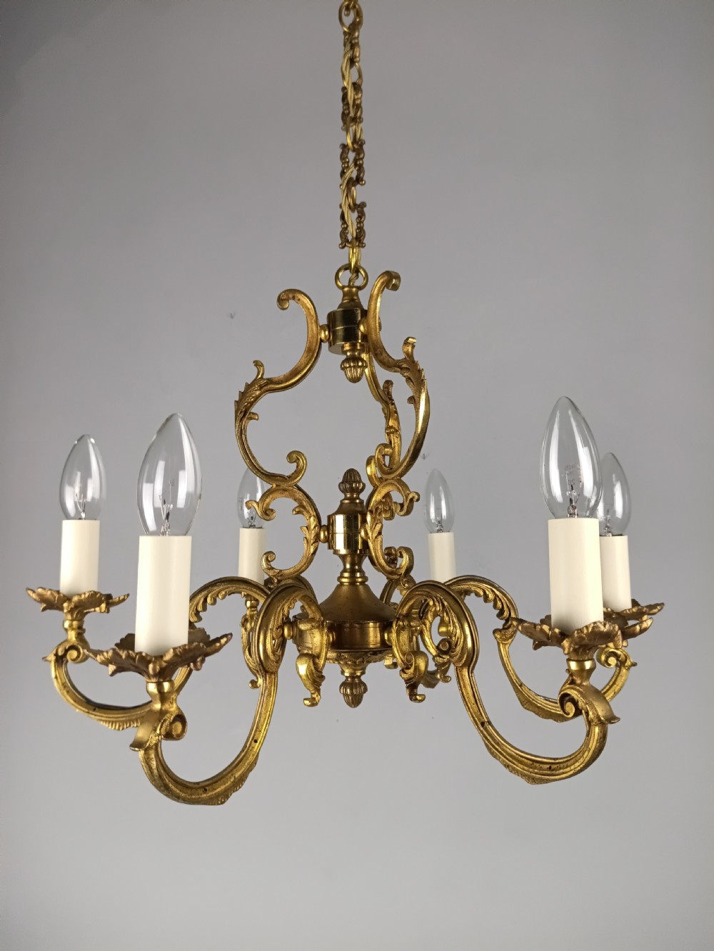 A six-arm French gilt brass chandelier featuring ornate acanthus scrollwork and white candle-style light sockets. View VI