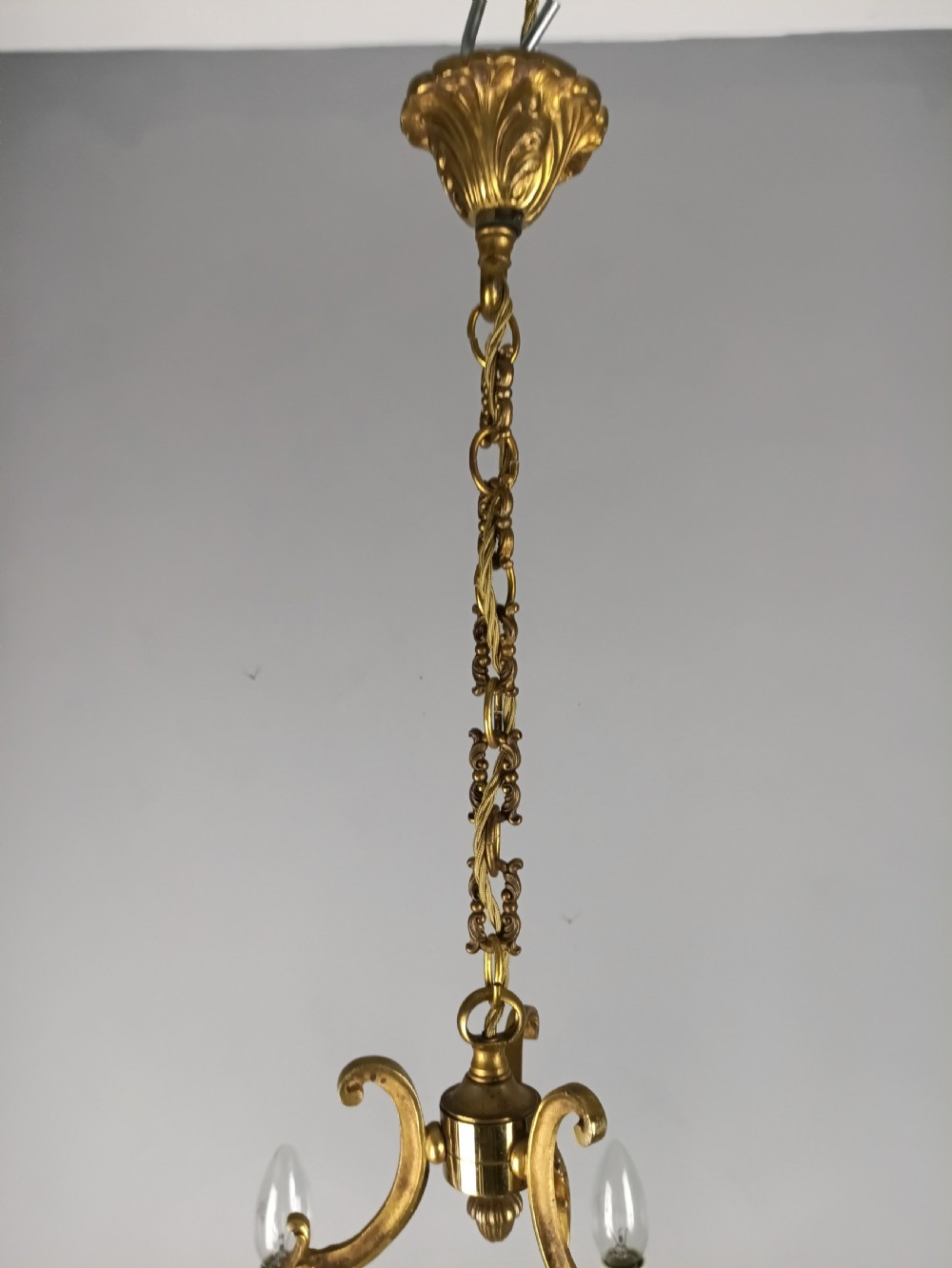 A six-arm French gilt brass chandelier featuring ornate acanthus scrollwork and white candle-style light sockets. View VII