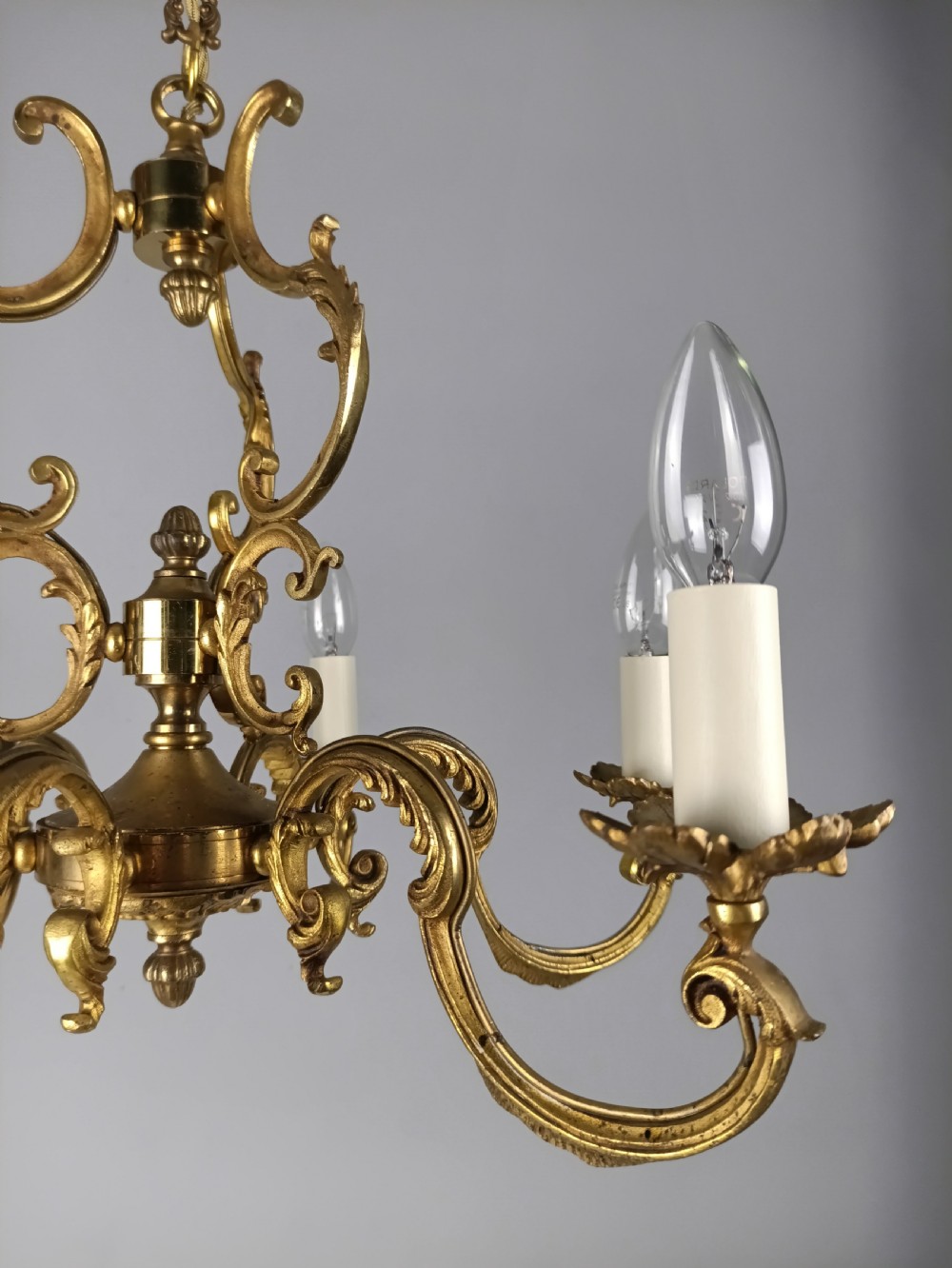A six-arm French gilt brass chandelier featuring ornate acanthus scrollwork and white candle-style light sockets. View IX