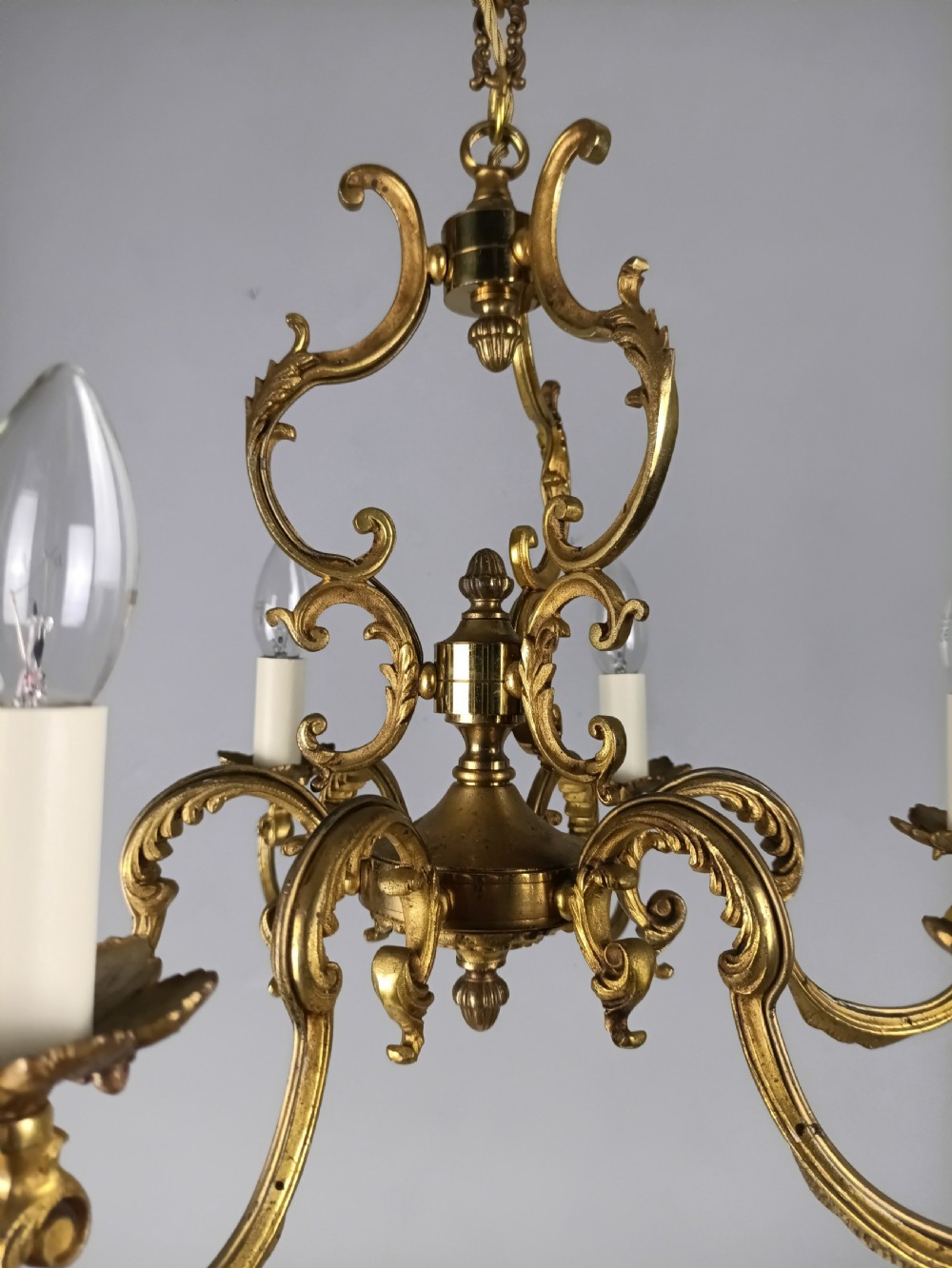 A six-arm French gilt brass chandelier featuring ornate acanthus scrollwork and white candle-style light sockets. View X