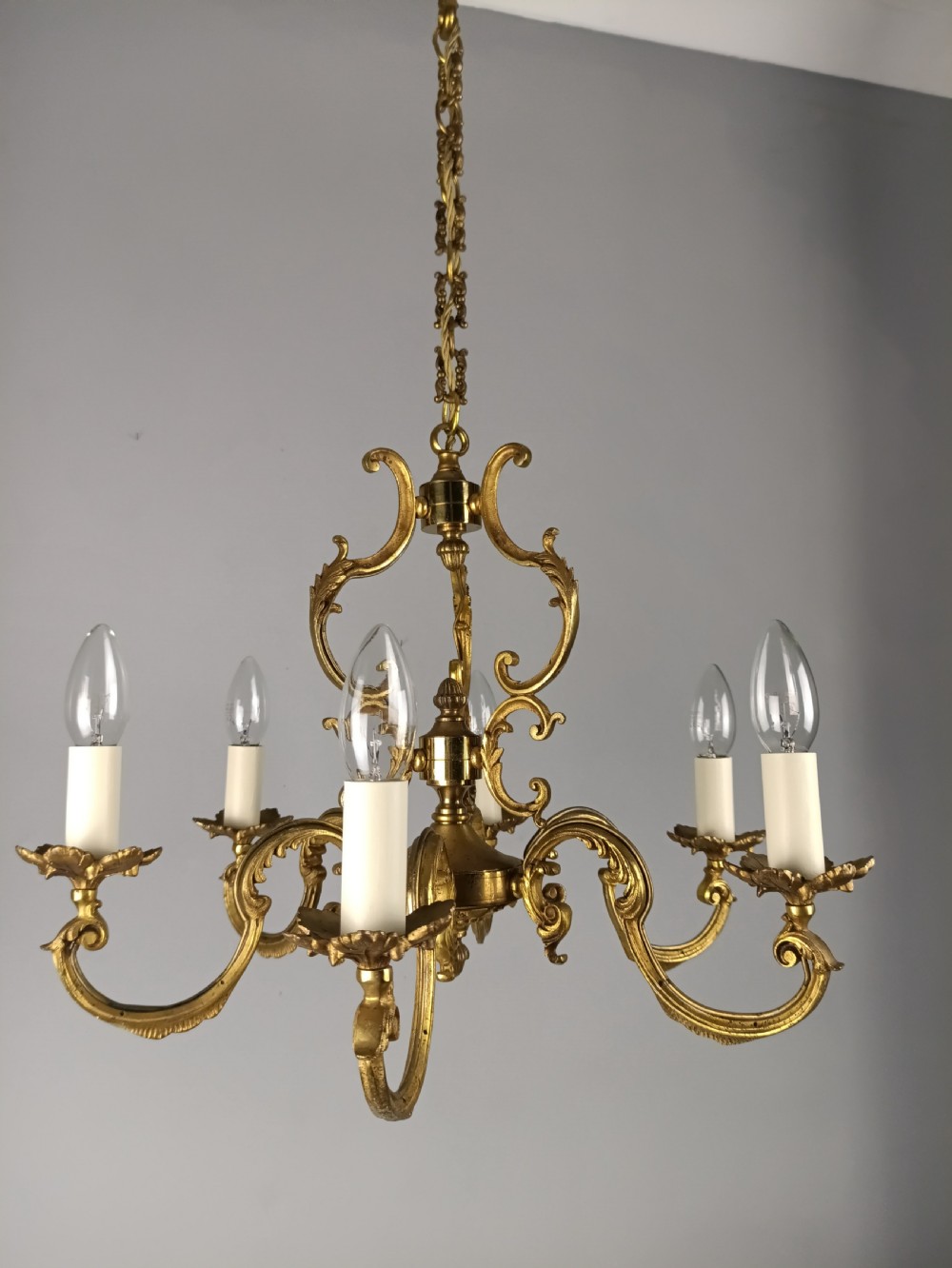 A six-arm French gilt brass chandelier featuring ornate acanthus scrollwork and white candle-style light sockets. View XI