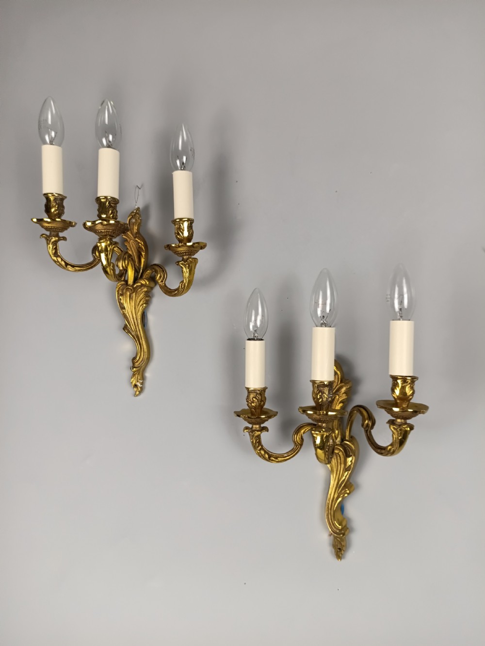 A pair of antique French Rococo wall sconces made from ornate gilded brass with three scrolling foliage-shaped arms each holding a candle-style light bulb. View III