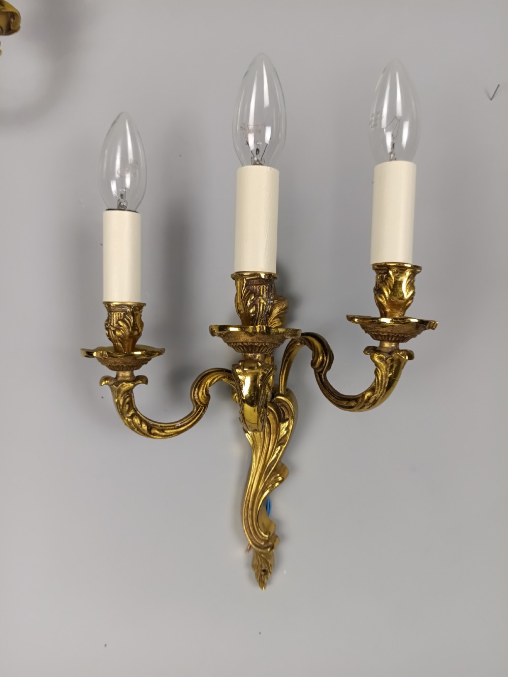 A pair of antique French Rococo wall sconces made from ornate gilded brass with three scrolling foliage-shaped arms each holding a candle-style light bulb. View VI