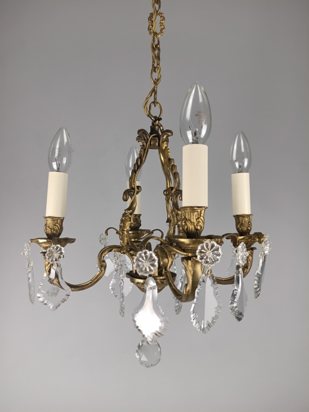 A four-arm French gilded brass chandelier adorned with cut crystal drops and cream candle-effect light holders.