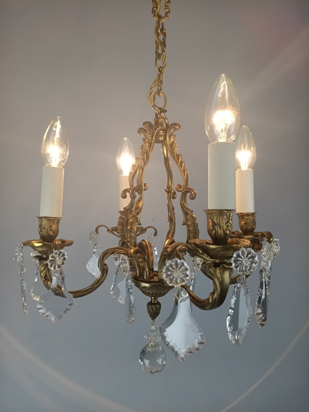 A four-arm French gilded brass chandelier adorned with cut crystal drops and cream candle-effect light holders. View V