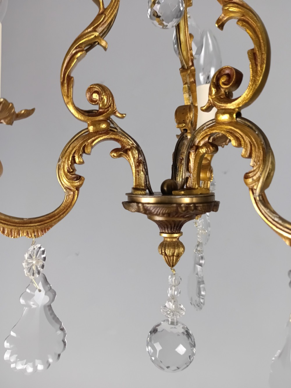 A French gilt bronze three-arm chandelier adorned with foliage scrollwork and hanging crystal droplets suspended from a ceiling chain. View II