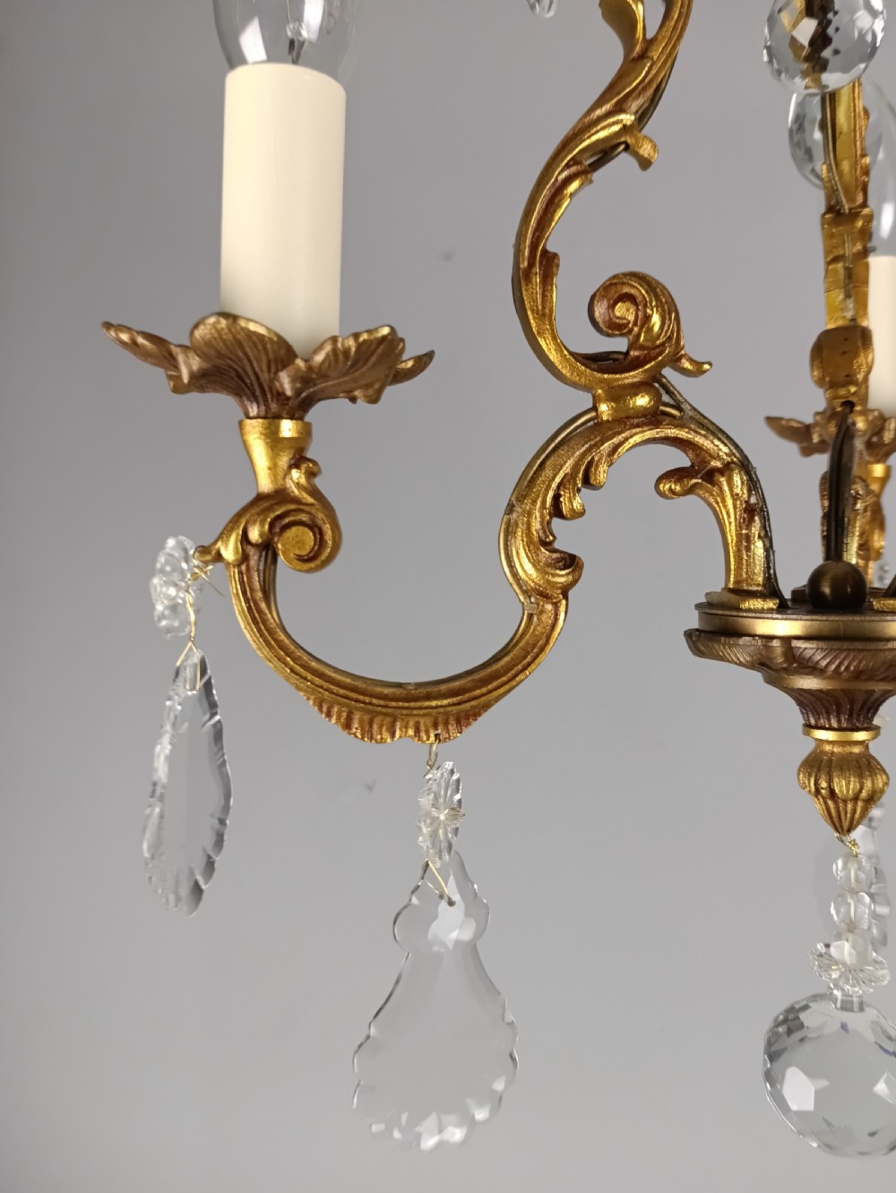 A French gilt bronze three-arm chandelier adorned with foliage scrollwork and hanging crystal droplets suspended from a ceiling chain. View III