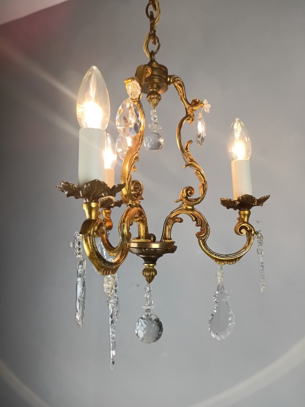 A French gilt bronze three-arm chandelier adorned with foliage scrollwork and hanging crystal droplets suspended from a ceiling chain. View V