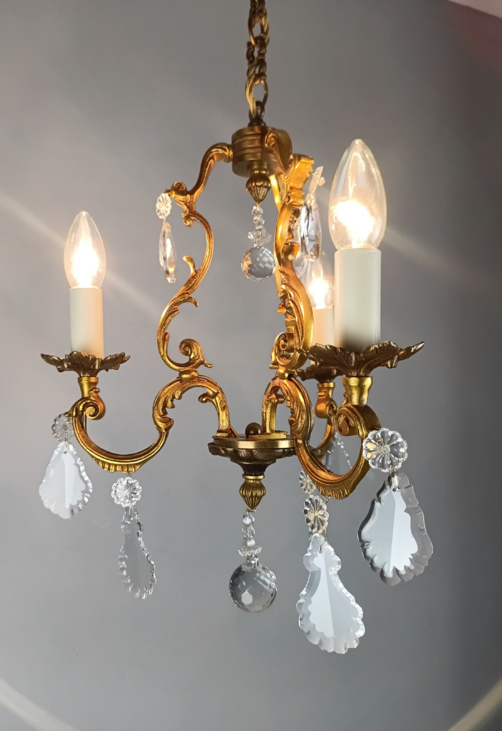 A French gilt bronze three-arm chandelier adorned with foliage scrollwork and hanging crystal droplets suspended from a ceiling chain. View VI