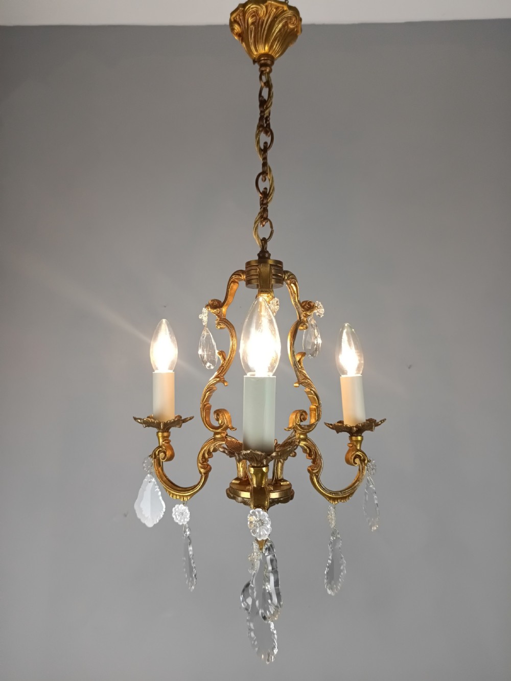 A French gilt bronze three-arm chandelier adorned with foliage scrollwork and hanging crystal droplets suspended from a ceiling chain. View VII