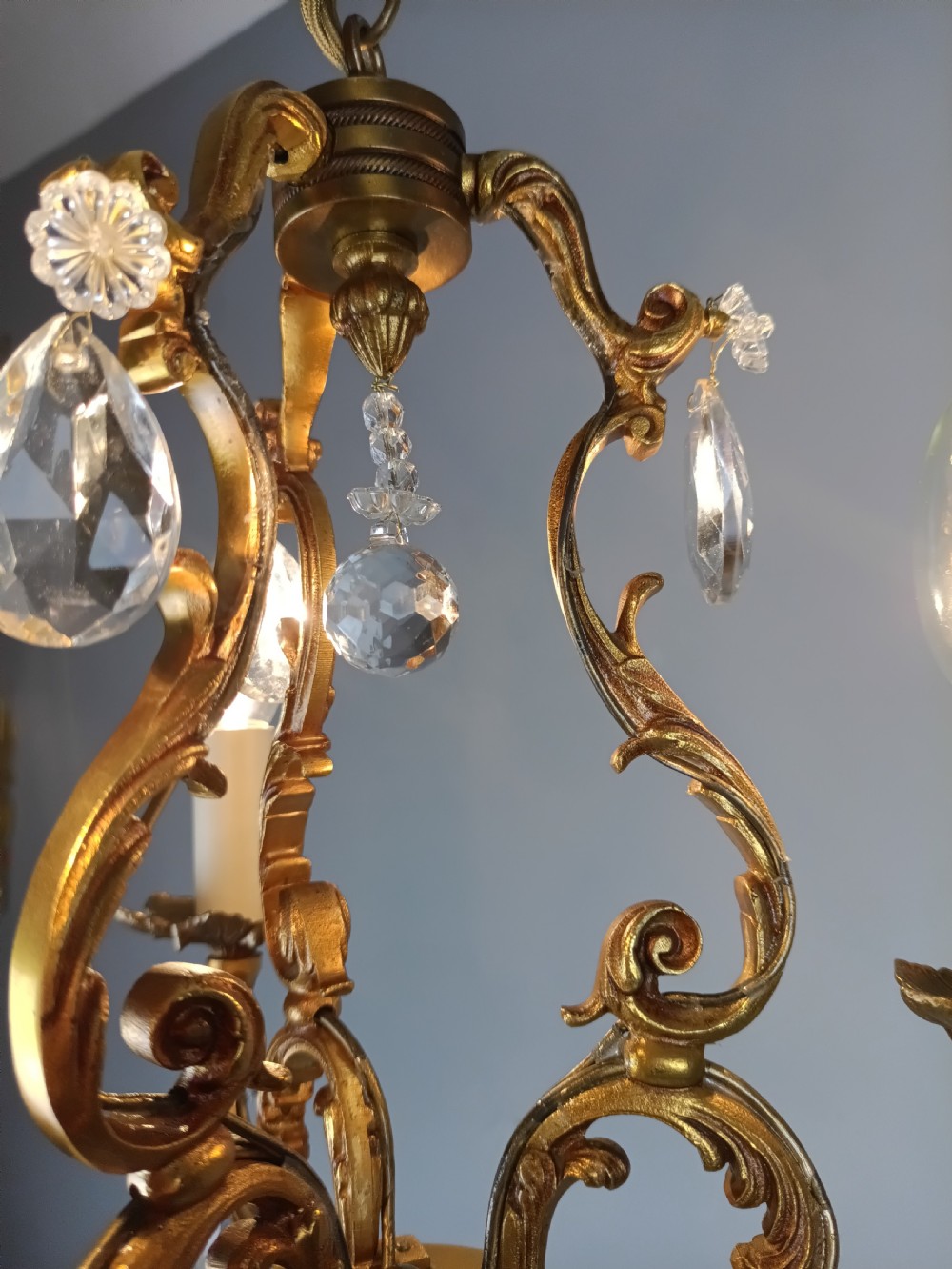 A French gilt bronze three-arm chandelier adorned with foliage scrollwork and hanging crystal droplets suspended from a ceiling chain. View IX