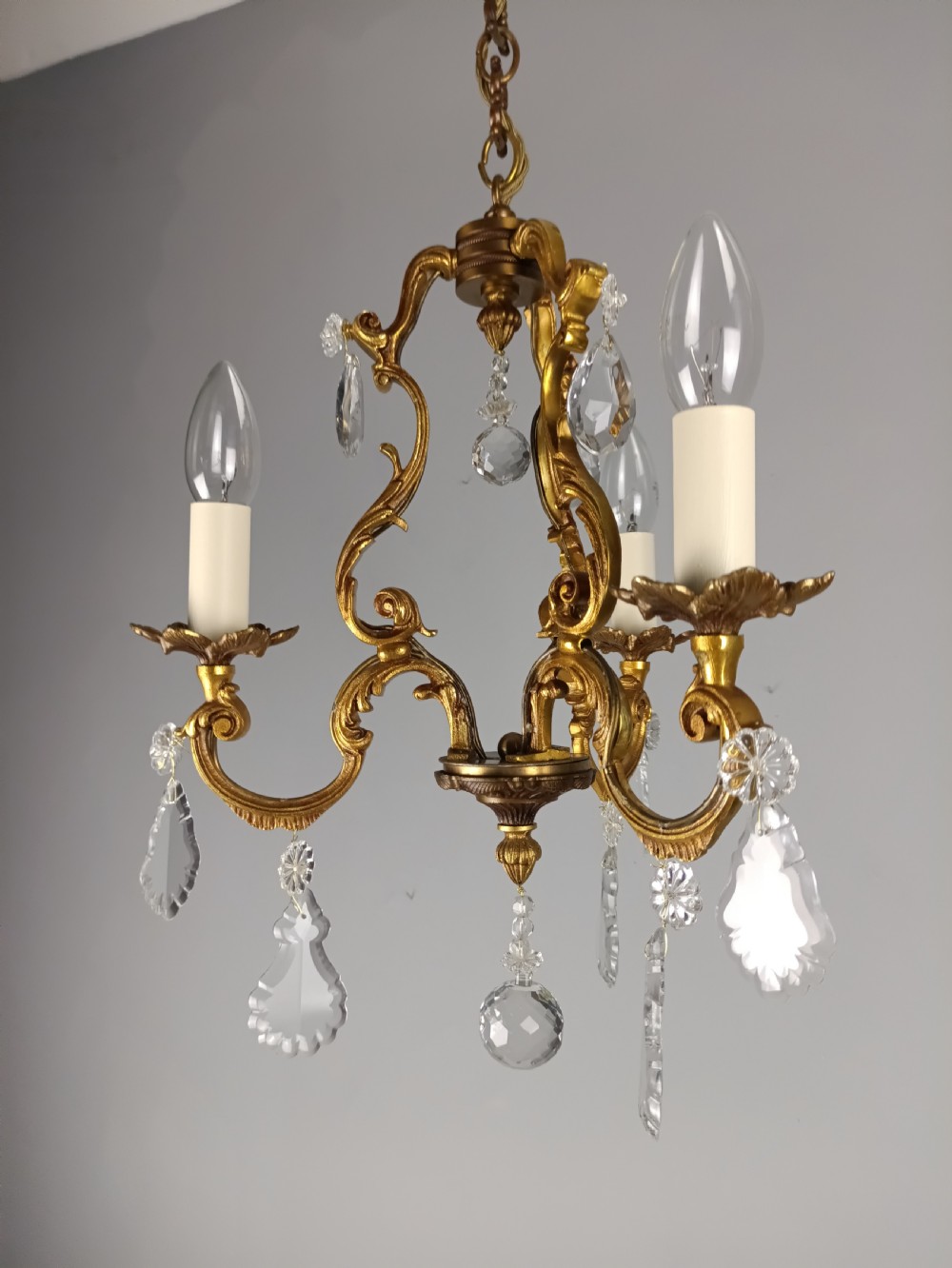 A French gilt bronze three-arm chandelier adorned with foliage scrollwork and hanging crystal droplets suspended from a ceiling chain. View X