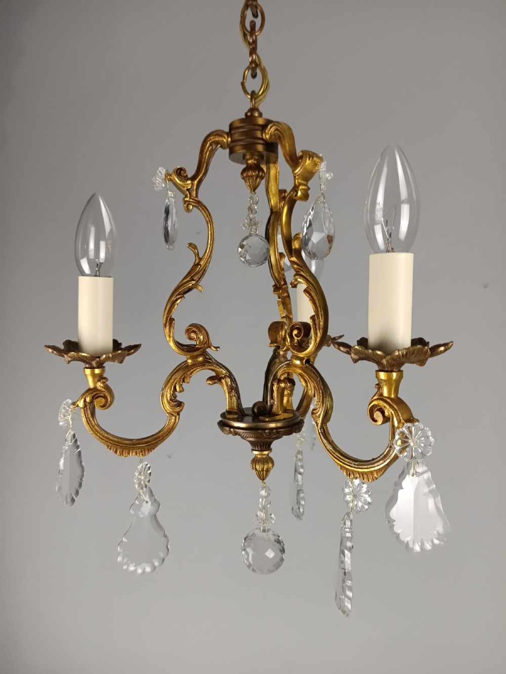 A French gilt bronze three-arm chandelier adorned with foliage scrollwork and hanging crystal droplets suspended from a ceiling chain. View XI