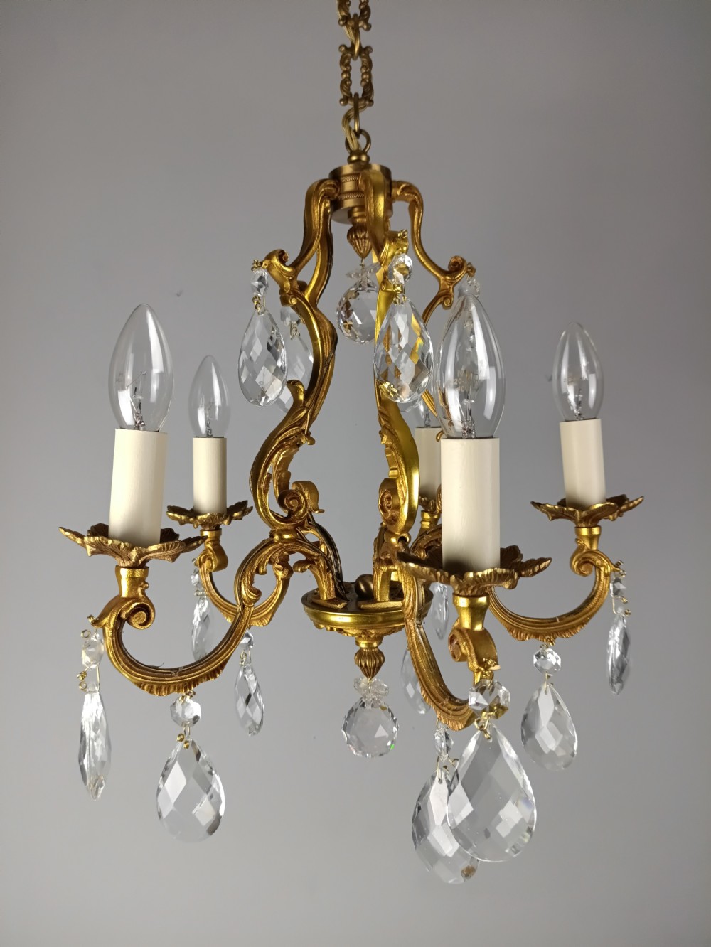 A French gilded brass five-arm chandelier featuring scrolling leaf motifs and faceted hanging crystal drops.