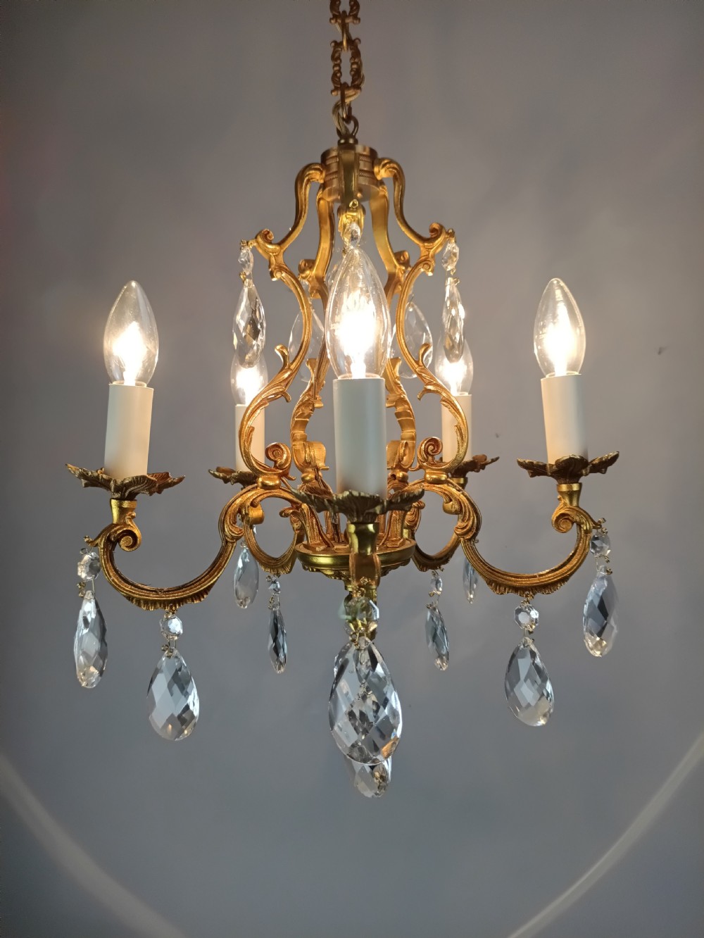 A French gilded brass five-arm chandelier featuring scrolling leaf motifs and faceted hanging crystal drops. View III