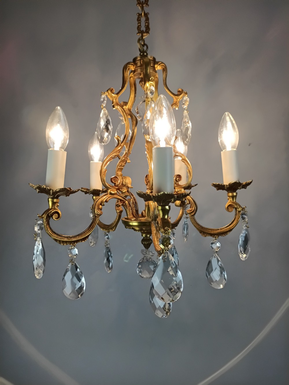 A French gilded brass five-arm chandelier featuring scrolling leaf motifs and faceted hanging crystal drops. View IV