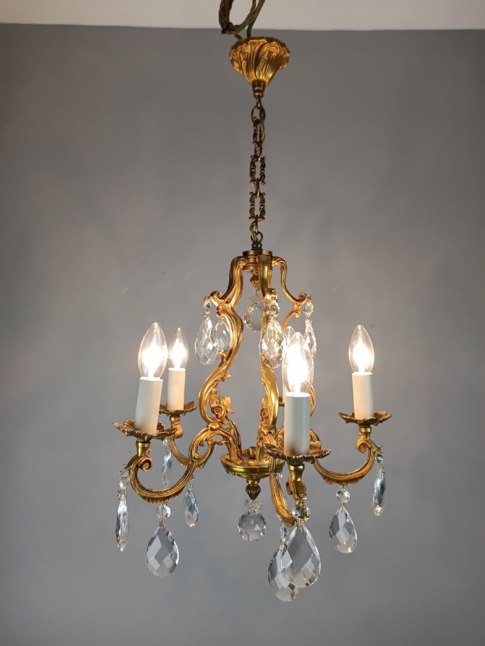 A French gilded brass five-arm chandelier featuring scrolling leaf motifs and faceted hanging crystal drops. View V