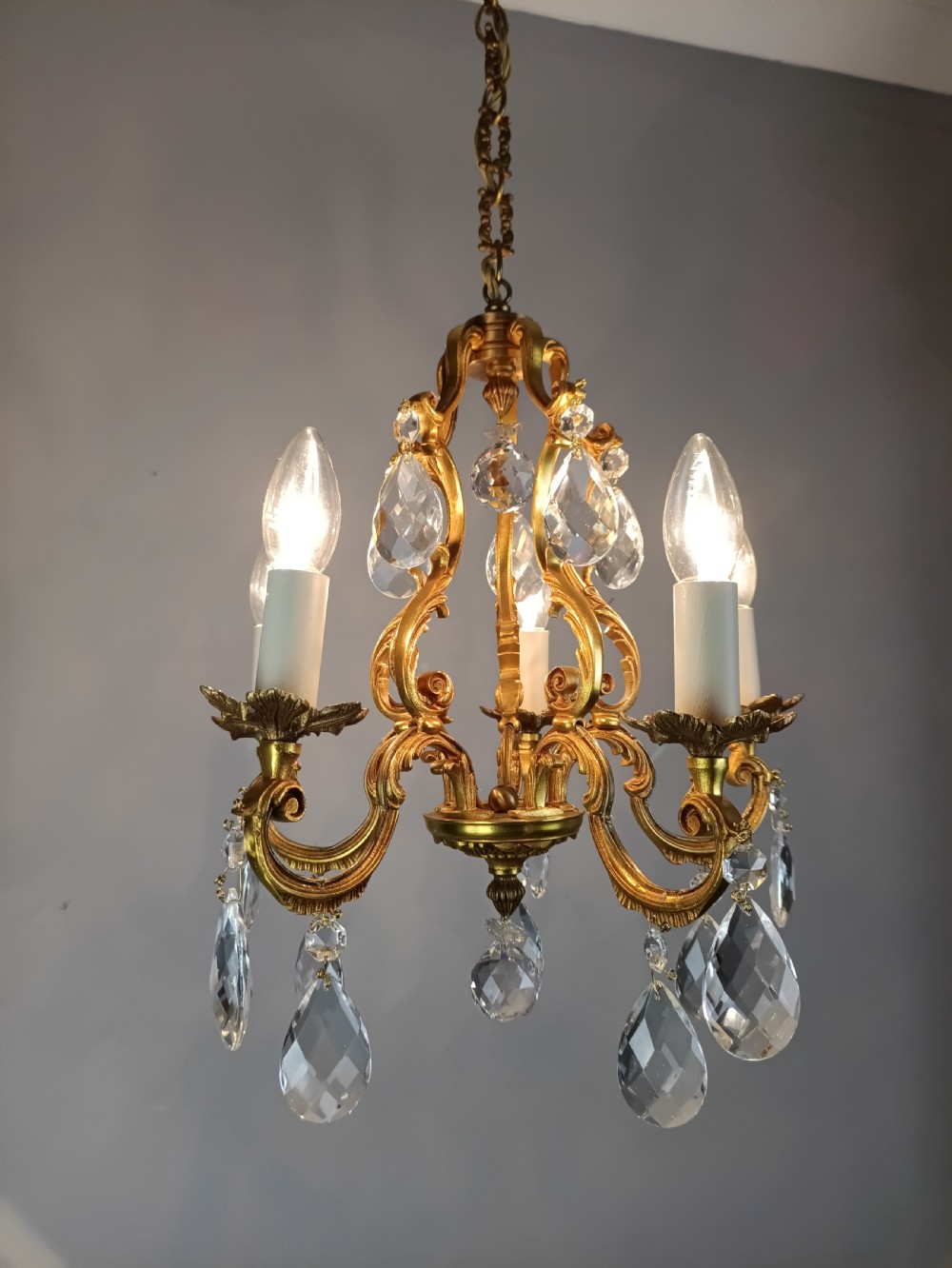 A French gilded brass five-arm chandelier featuring scrolling leaf motifs and faceted hanging crystal drops. View VI