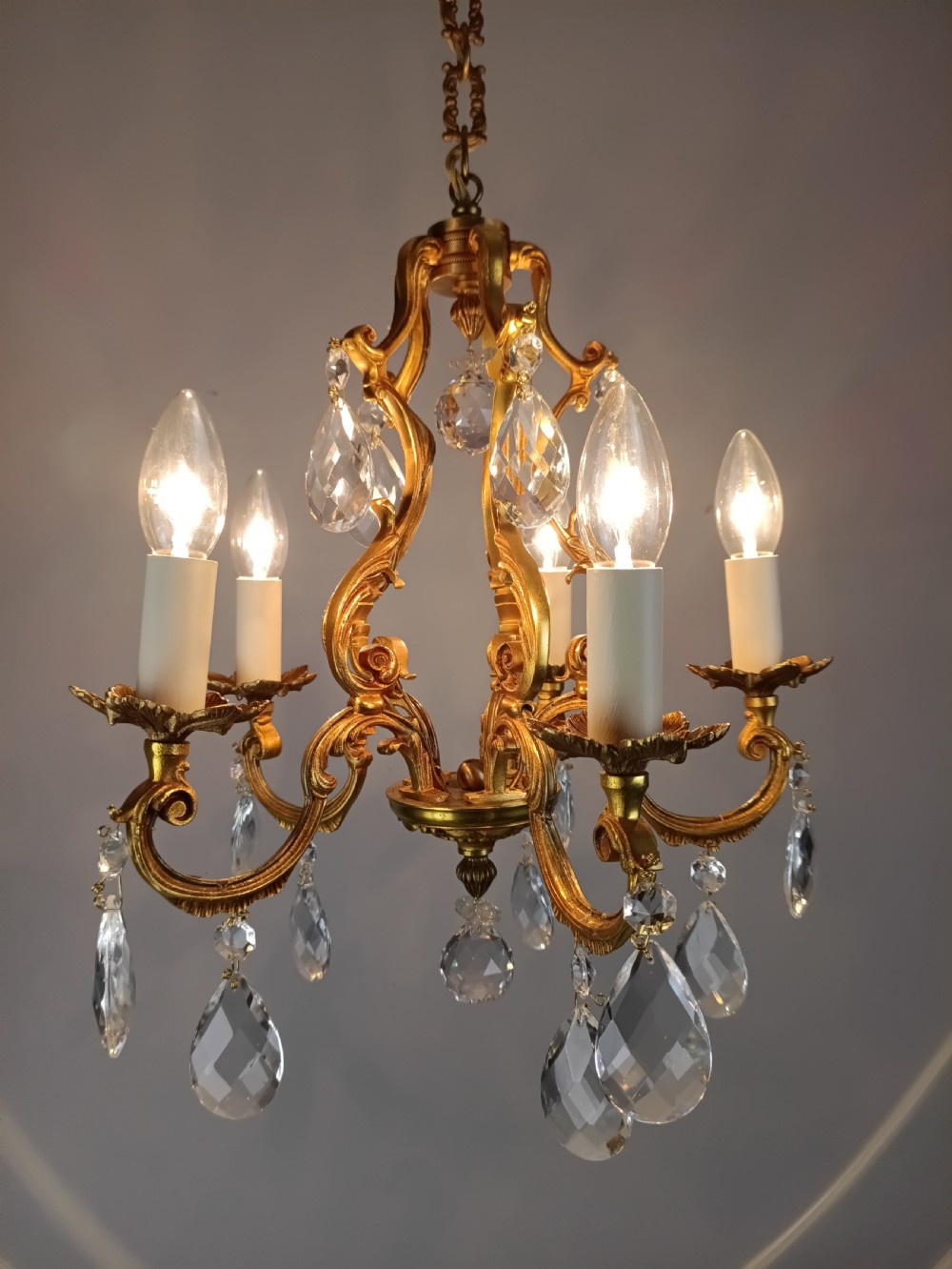 A French gilded brass five-arm chandelier featuring scrolling leaf motifs and faceted hanging crystal drops. View VII