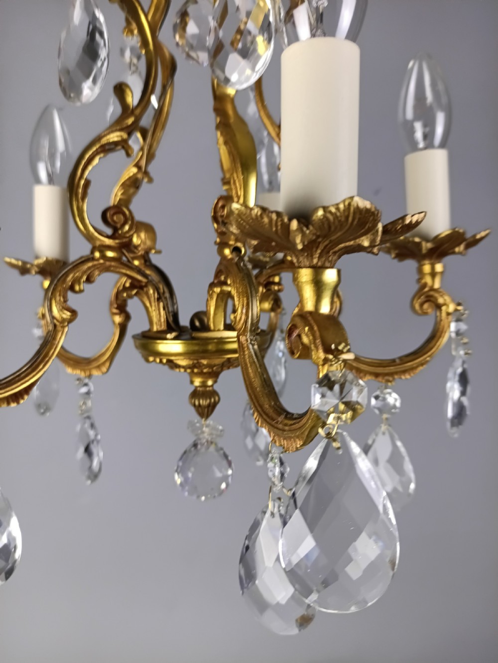 A French gilded brass five-arm chandelier featuring scrolling leaf motifs and faceted hanging crystal drops. View VIII