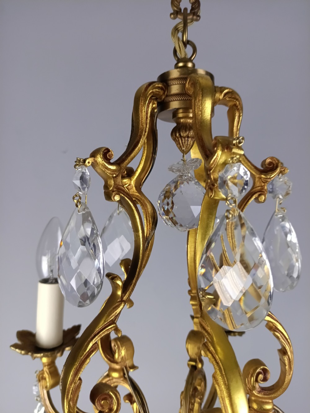 A French gilded brass five-arm chandelier featuring scrolling leaf motifs and faceted hanging crystal drops. View IX