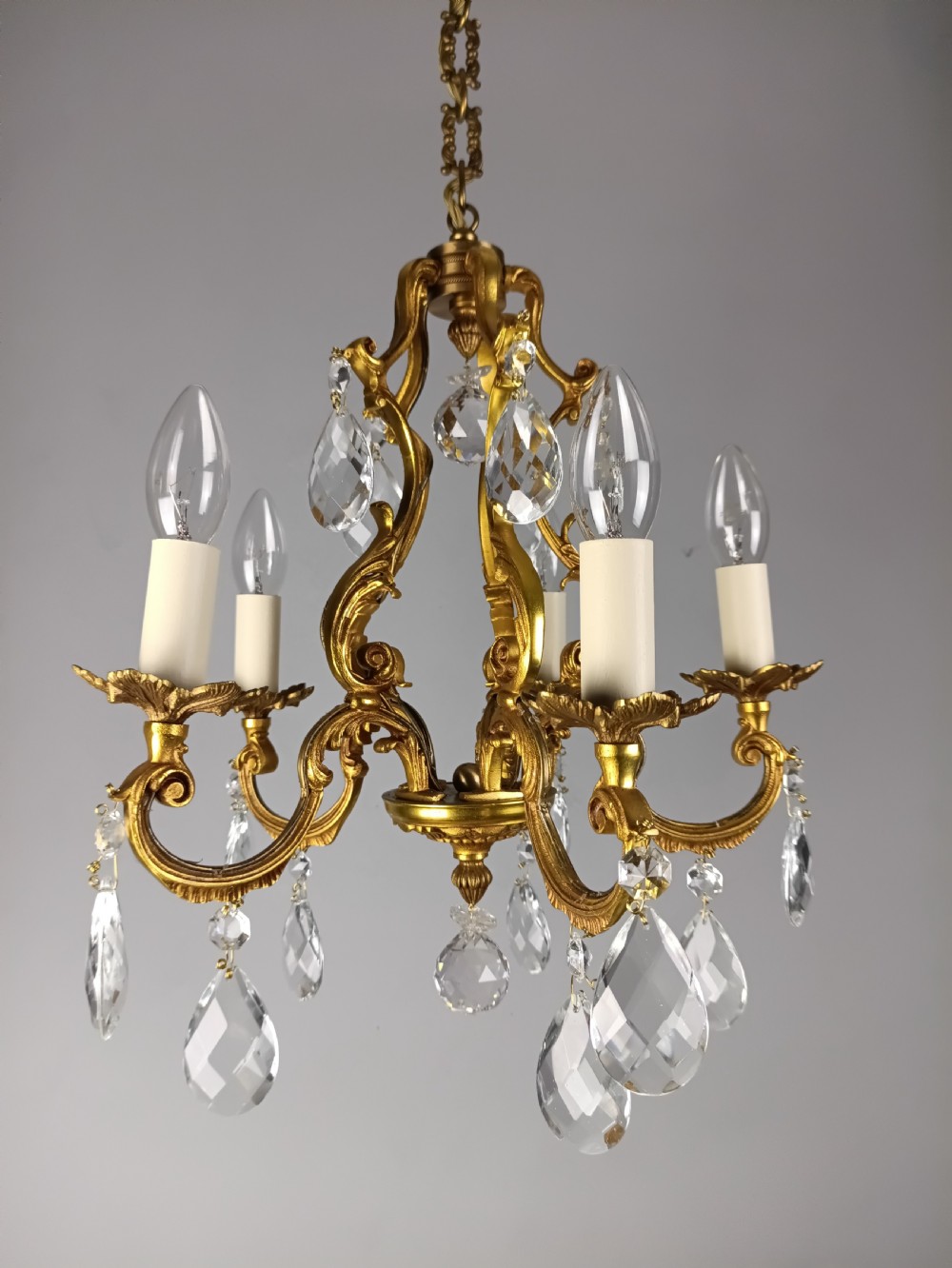 A French gilded brass five-arm chandelier featuring scrolling leaf motifs and faceted hanging crystal drops. View X