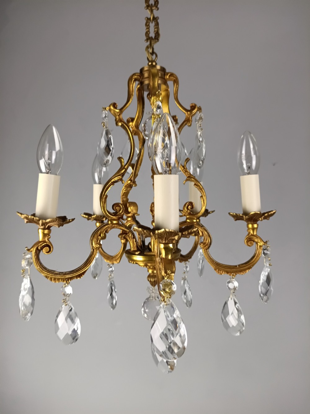 A French gilded brass five-arm chandelier featuring scrolling leaf motifs and faceted hanging crystal drops. View XI