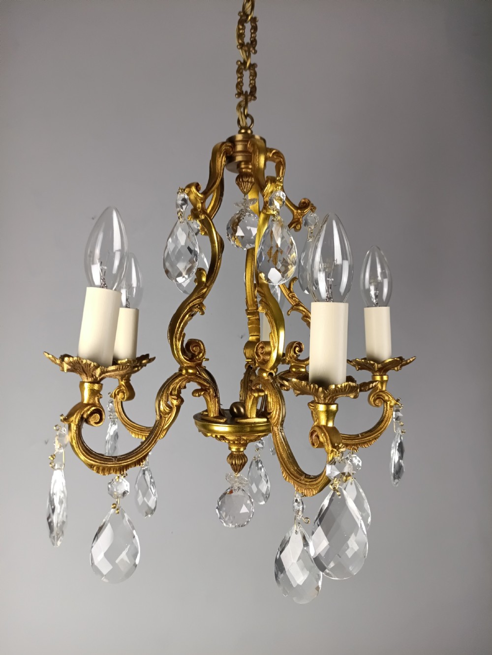 A French gilded brass five-arm chandelier featuring scrolling leaf motifs and faceted hanging crystal drops. View XIII