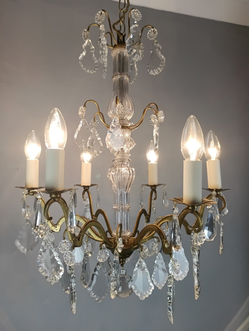 A French style gilt brass six arm chandelier embellished with clear glass stem sections and suspended crystal teardrop prisms. View II