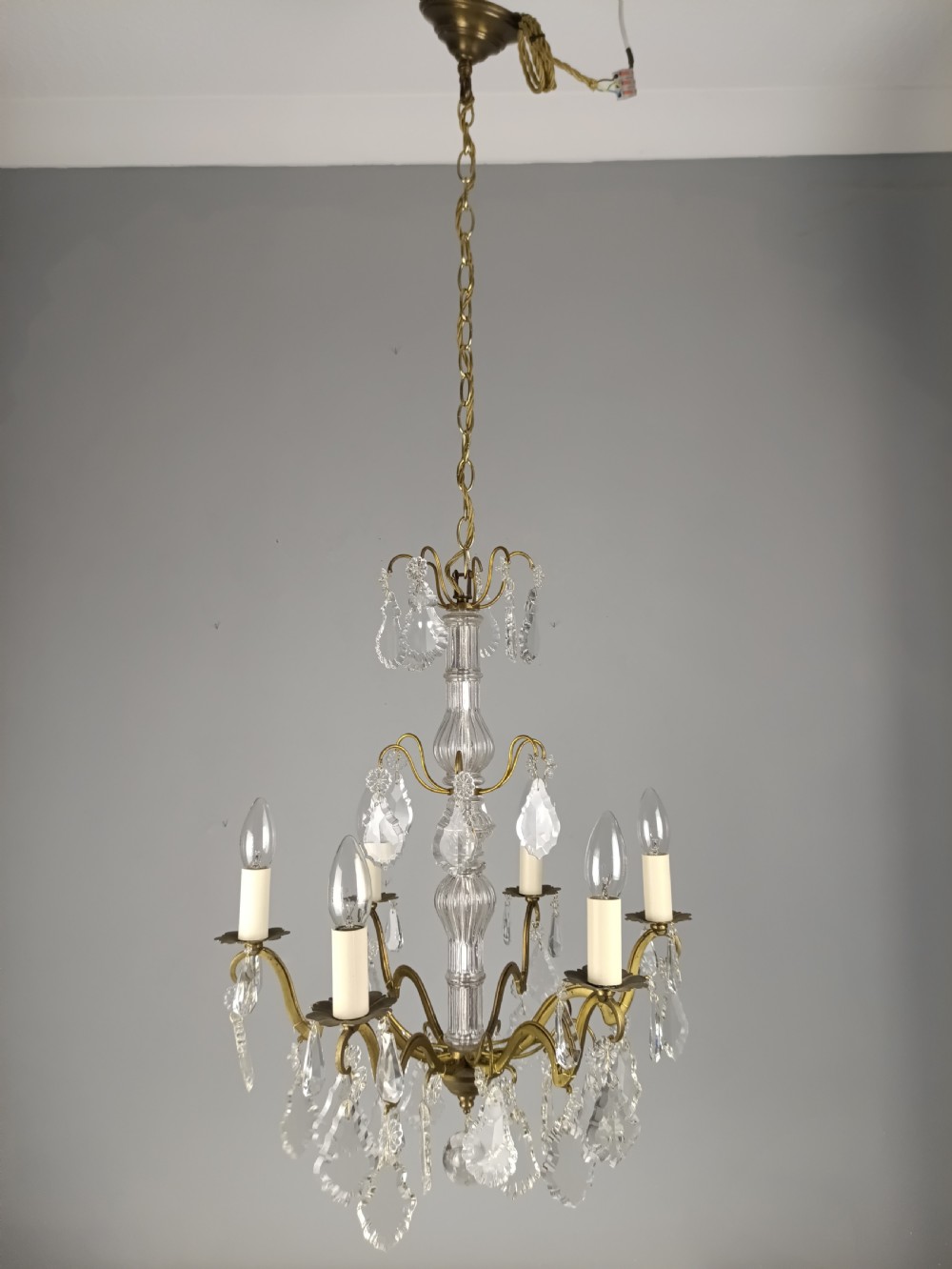 A French style gilt brass six arm chandelier embellished with clear glass stem sections and suspended crystal teardrop prisms. View IV