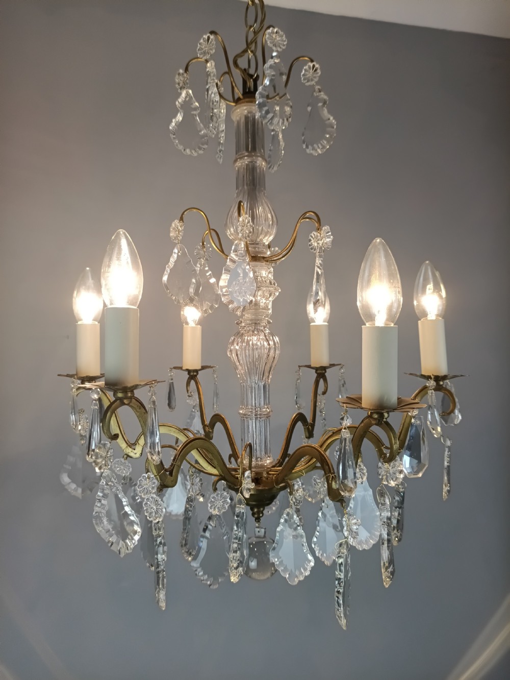 A French style gilt brass six arm chandelier embellished with clear glass stem sections and suspended crystal teardrop prisms. View V