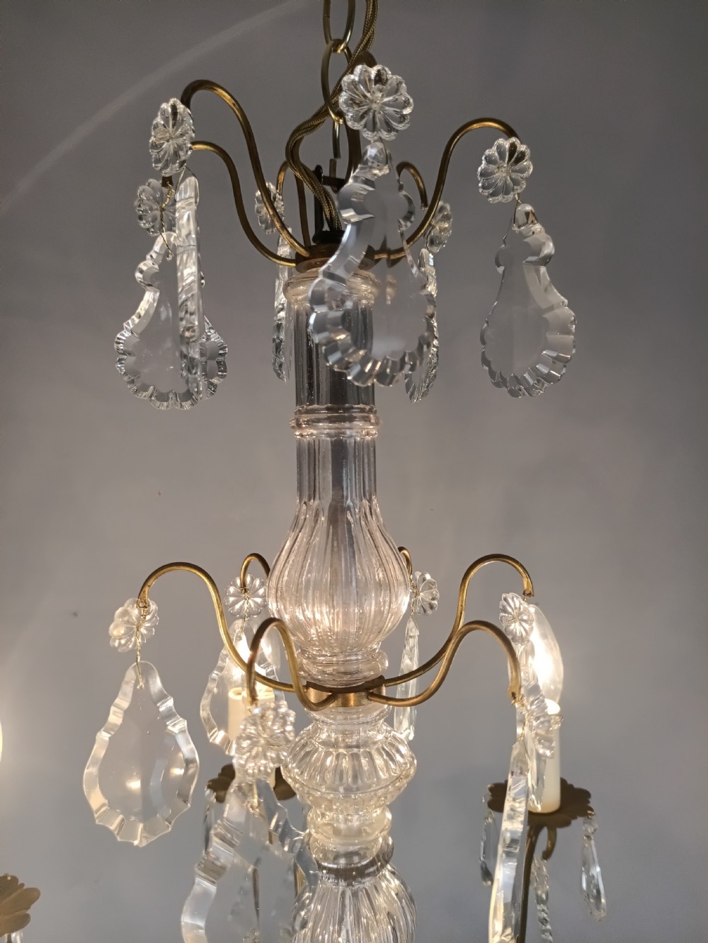 A French style gilt brass six arm chandelier embellished with clear glass stem sections and suspended crystal teardrop prisms. View VII