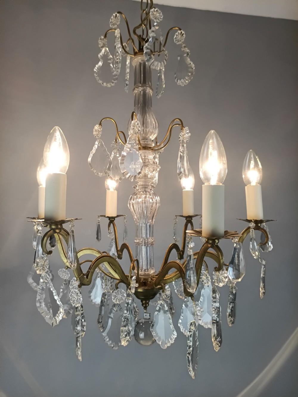 A French style gilt brass six arm chandelier embellished with clear glass stem sections and suspended crystal teardrop prisms. View VIII