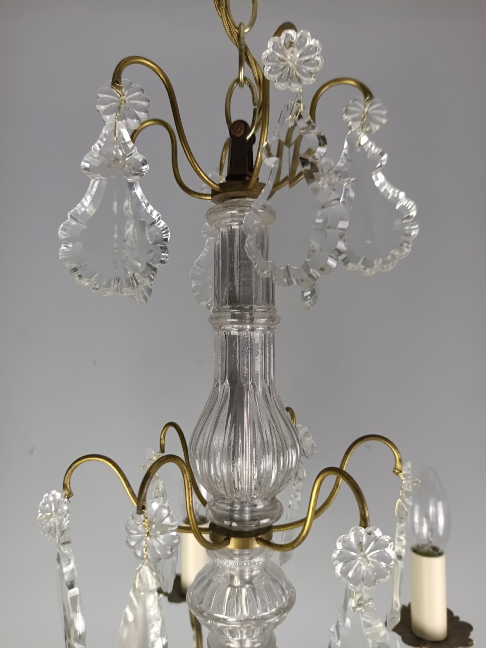 A French style gilt brass six arm chandelier embellished with clear glass stem sections and suspended crystal teardrop prisms. View X